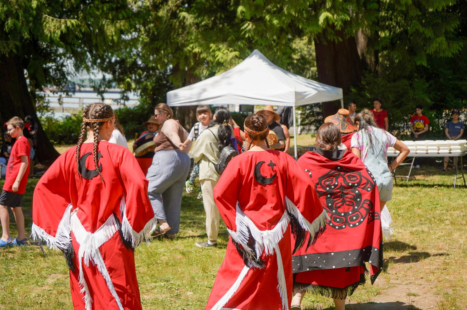 Dancers in red regalia at an outdoor summer camp gathering